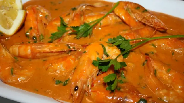 Shrimp in a thick orange sauce with parsley leaves and a lemon wedge at the side