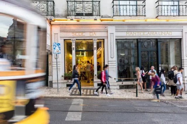 A gold-lit shopfront on a city street, passers-by and a blurred yellow tram