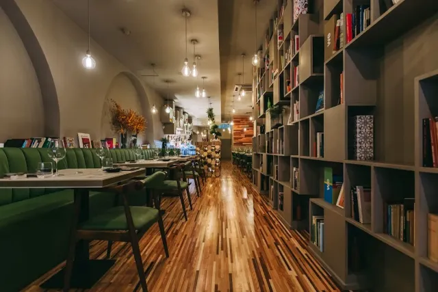 An aisle with a wall of bookshelves, green benches and a light wooden floor