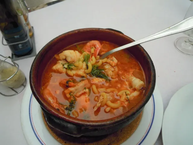 A clay pot with tomato soup, short pasta and seafood, a spoon inside it