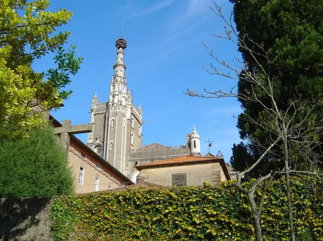 An ornate Manueline style tower rising above a hedge and trees