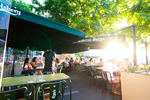 A busy terrace under green parasols with sunlight coming through the trees