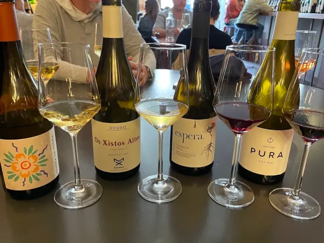 A row of wine bottles and glasses of white and red wine on a dark bar counter