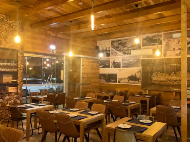 A wood-clad hall with hanging bulbs, set tables and old harbour photographs on the wall