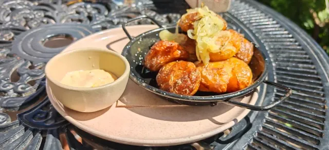 A small pan with fried sausage and onion beside a bowl of sauce on a metal table