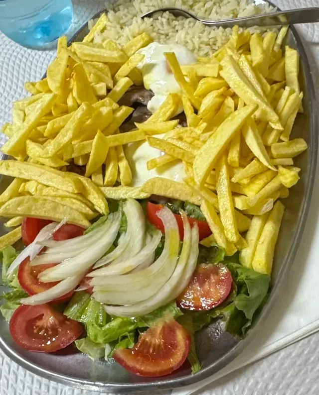 A metal platter with chips, rice, a fried egg and a salad of tomatoes, lettuce and onion
