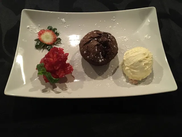 A dessert plate with a chocolate cake, a scoop of ice cream and sliced strawberries on a dark background