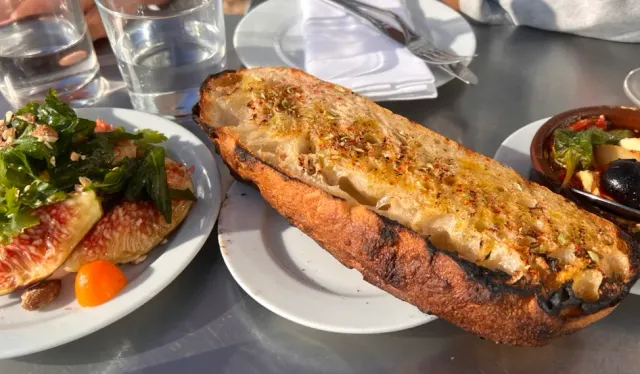 An open sandwich in toasted bread with cheese, beside a fig salad and a bowl of olives