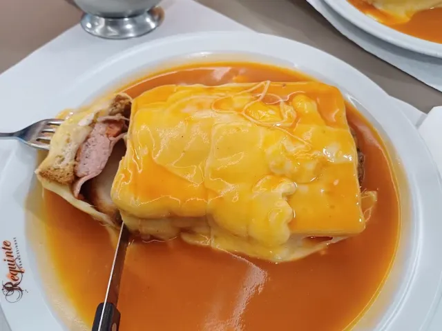 A cut sandwich covered in melted cheese in a thick orange sauce on a white plate
