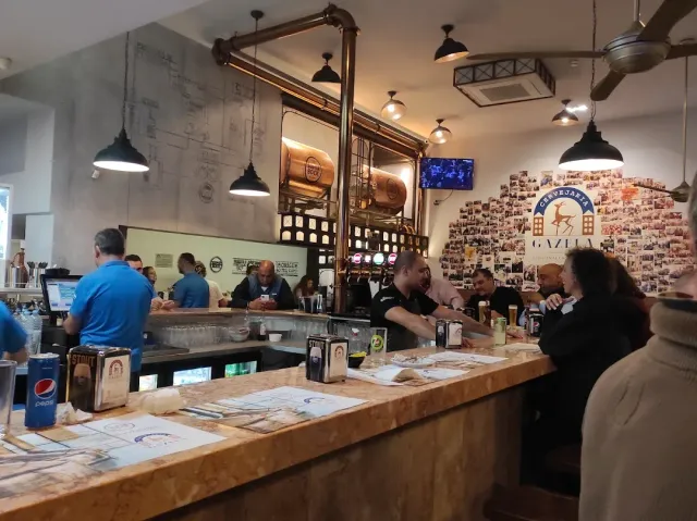 A long wooden counter with diners, a copper vessel and a wall covered in small photographs