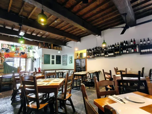 A room with a beamed ceiling, green glass lamps and shelves of wine bottles