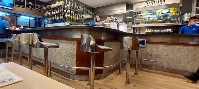 A curved counter with metal stools, shelves of bottles and staff behind the bar