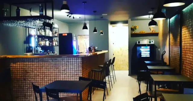 A tiled bar counter with high stools, hanging lamps and blue lighting