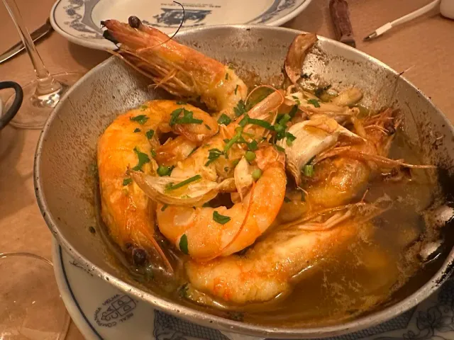 A metal pan with shrimp in garlic sauce and parsley on a patterned plate