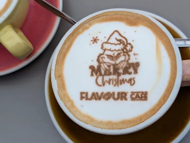 A cup of coffee with white foam topped with a Christmas illustration in cocoa powder