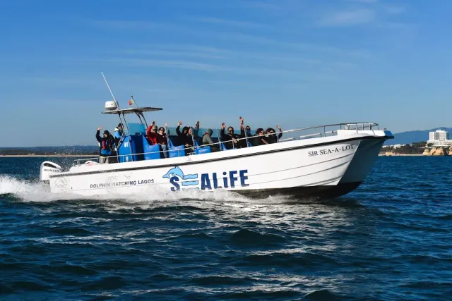 A white tour boat cutting through the sea, passengers waving from the deck