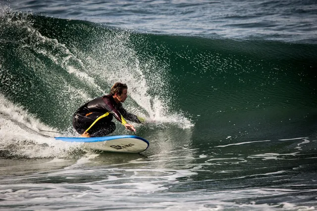 A surfer in a black wetsuit carving a green wave amid spray
