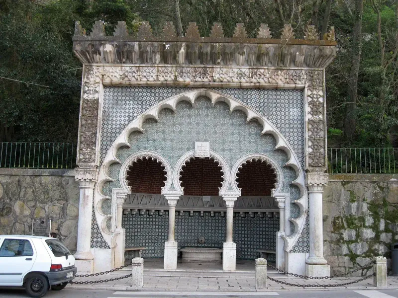 An arched Moorish-style wall fountain, tiled in green and white and surrounded by trees
