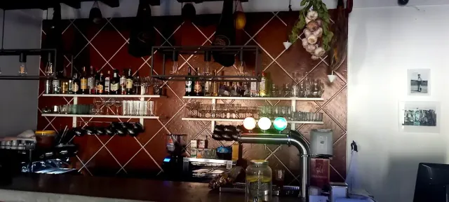 A bar back with bottle shelves, hanging glasses, a garlic braid and a drinks tap