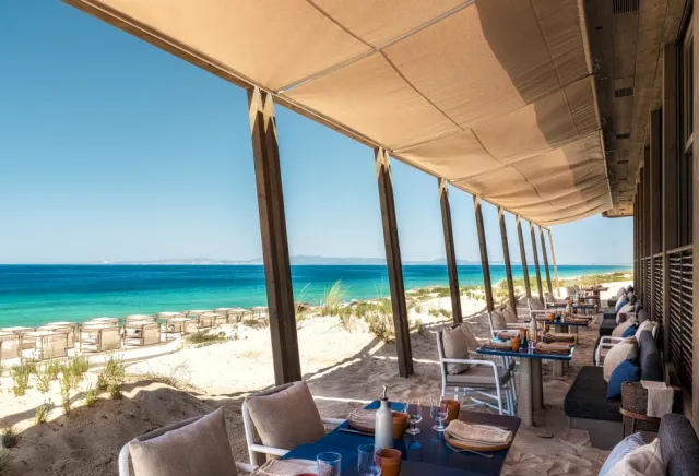 A canvas covered deck over the sand, set tables and turquoise water behind