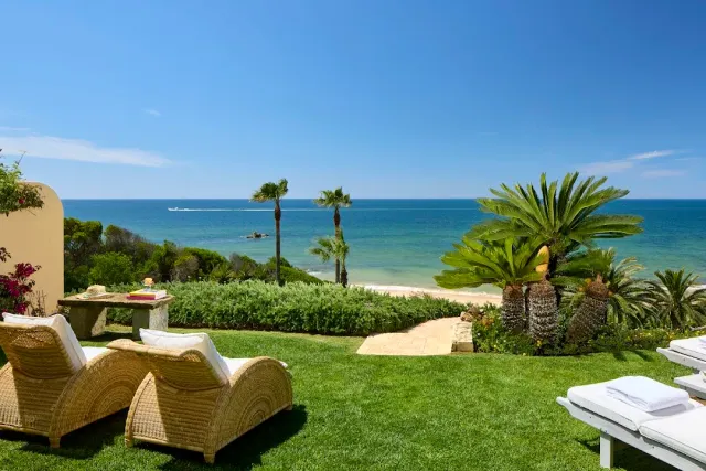 A lawn with woven sun loungers, palm trees and a blue sea on the horizon