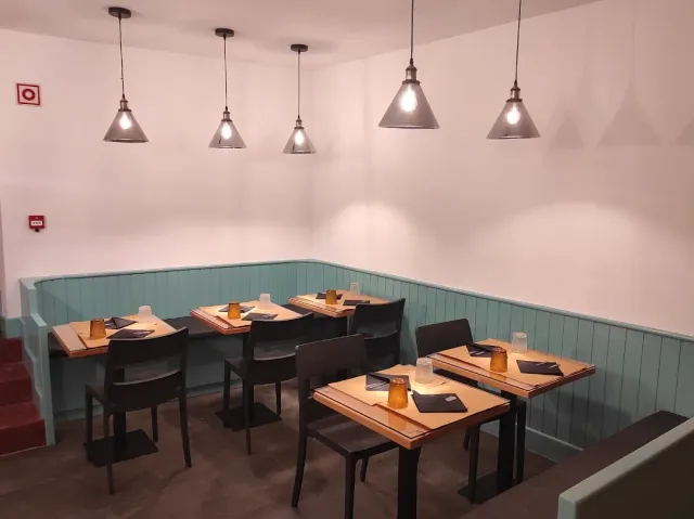 A small room with a light blue wooden bench, hanging lamps and wooden tables