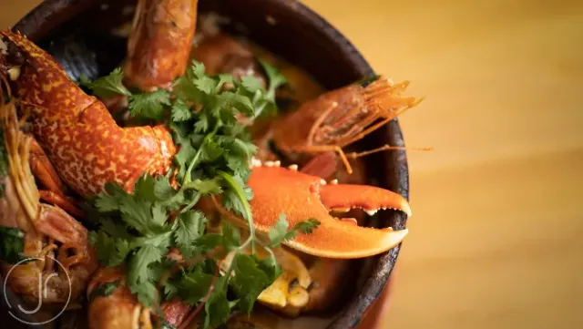 A close up of a clay pot with lobster, prawns, a crab claw and green coriander