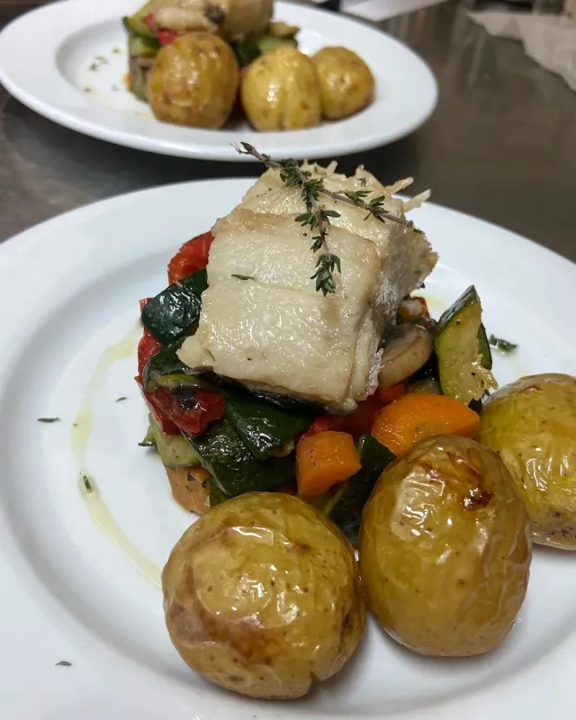 A white fish fillet over roasted vegetables and small potatoes on a plate