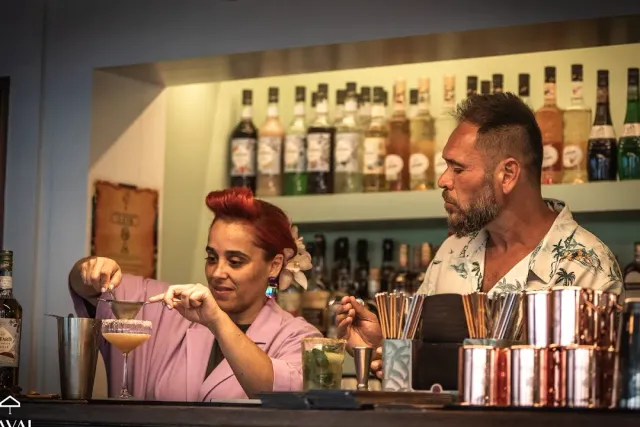 Two bartenders making drinks behind the counter facing a bottle shelf