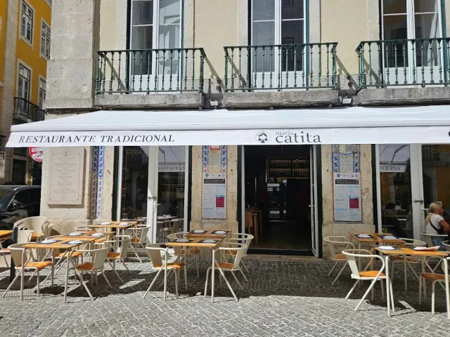 A restaurant front with a white awning, outdoor tables and a stone paved square