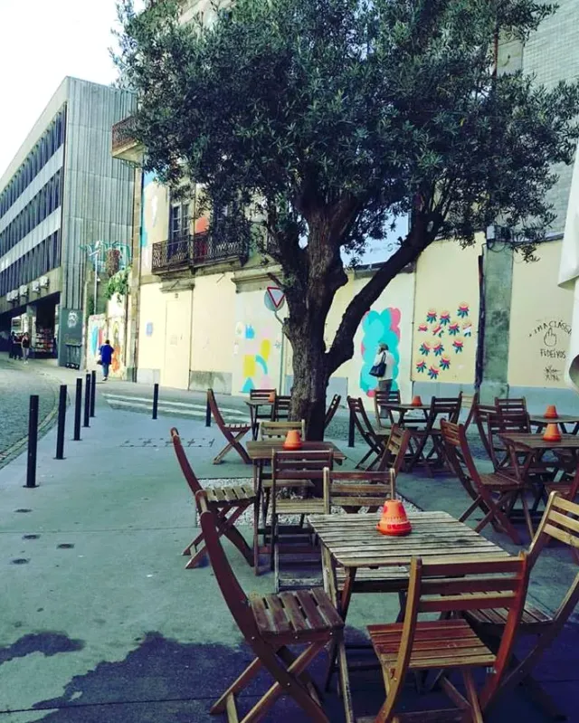 Folding wooden chairs and tables on the street, an olive tree and walls with murals