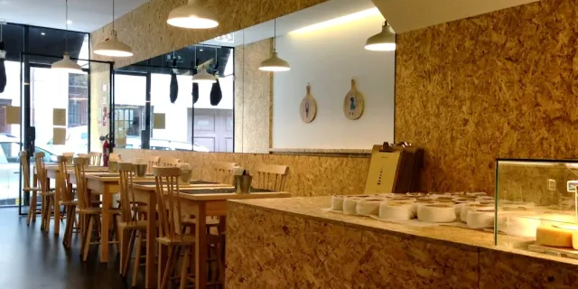 A space with wooden board walls, a counter with small white bowls and tall stools
