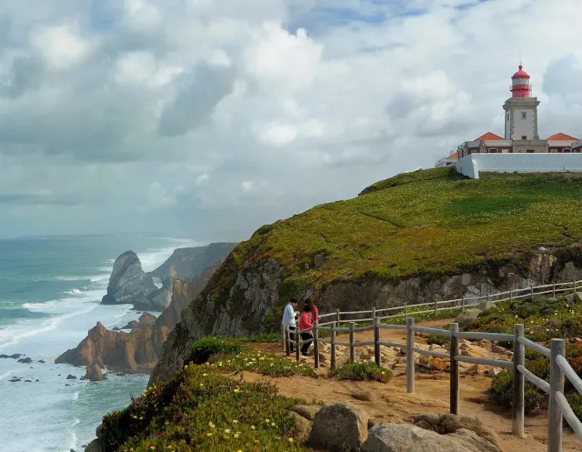 A lighthouse on a high green cliff above the ocean with a boardwalk below