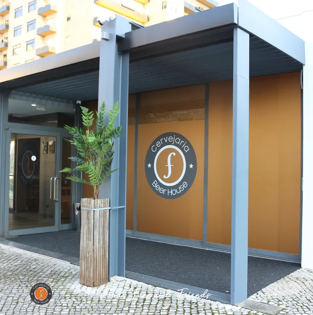 A covered entrance with a round logo on an orange wall and a fern pot by the door