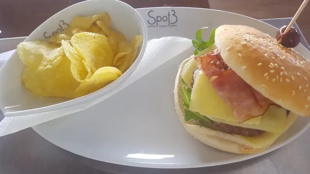 A burger with cheese and bacon beside a bowl of chips on a white plate