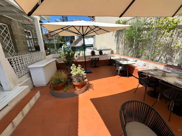 A terracotta tiled terrace with beige parasols, potted plants and black rattan chairs