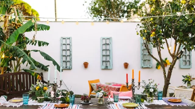 A set table in a courtyard with a candelabra, flowers and a lemon tree against a white wall