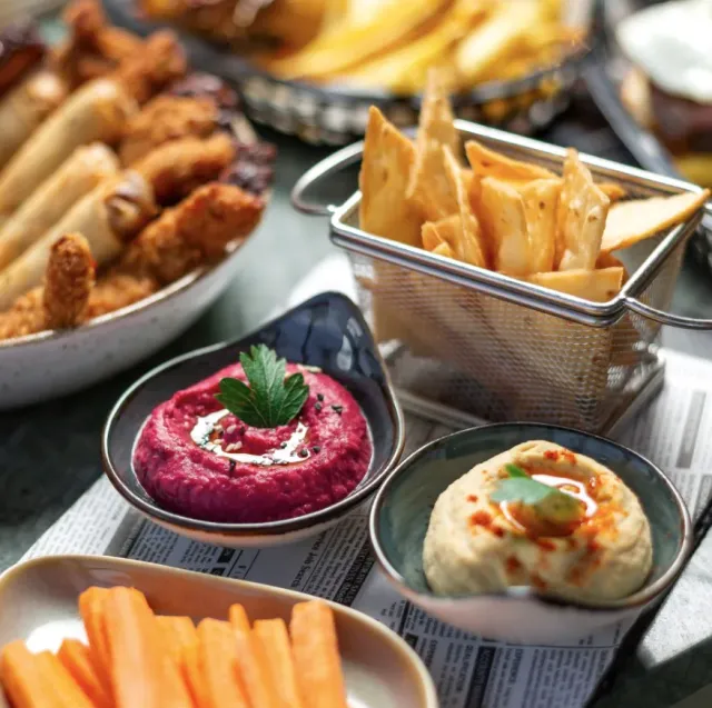 Starters in small bowls with beet spread, hummus, carrots and baked crisps