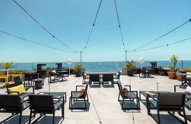 An open rooftop with black armchairs, string lights and the sea on the horizon
