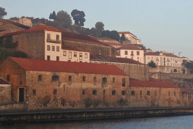 Old stone warehouses with red tiled roofs on the riverbank, as seen from the water