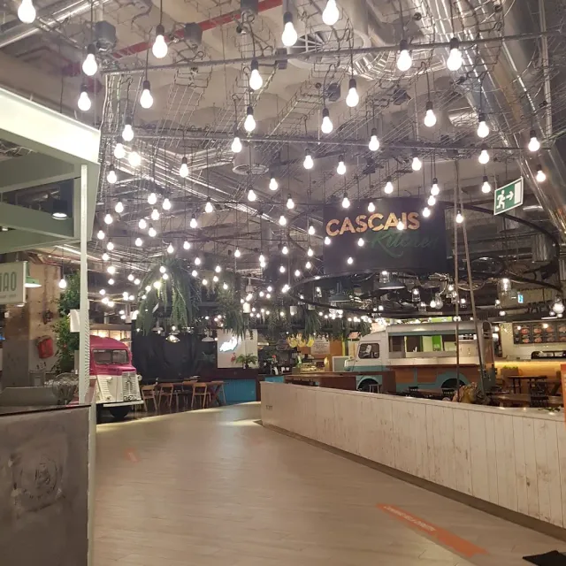 A food court with dozens of bulbs hanging from the ceiling and van shaped stalls