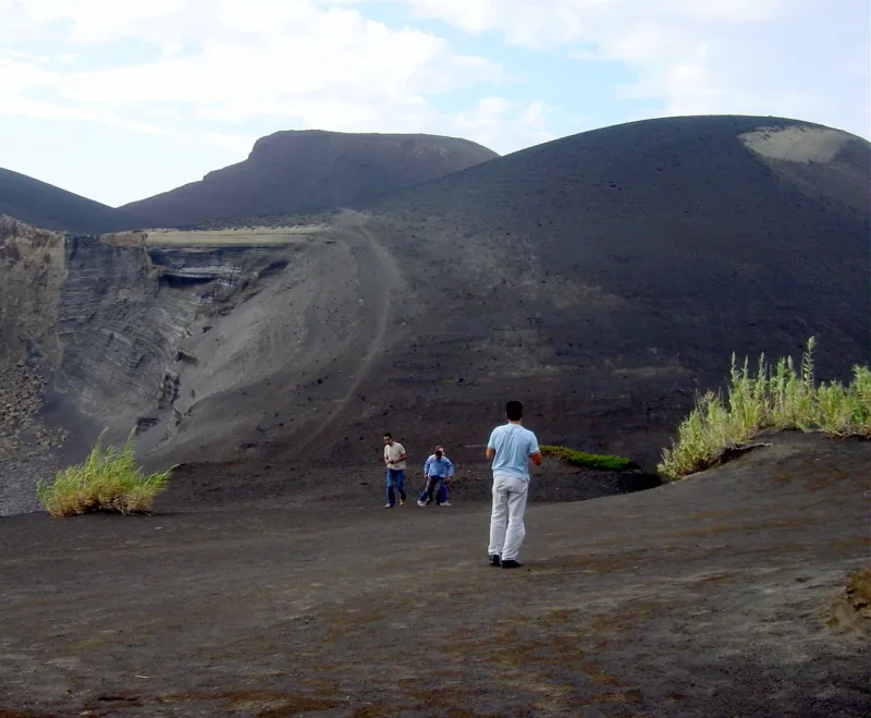 Bare black volcanic ash hills with a few tiny walkers at their edge