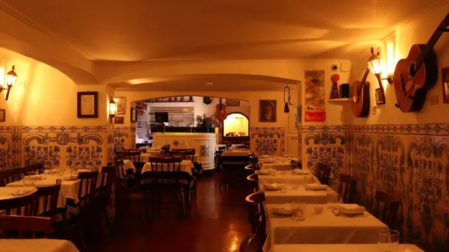 A dim room with painted tiles on the walls, hanging guitars and white tables