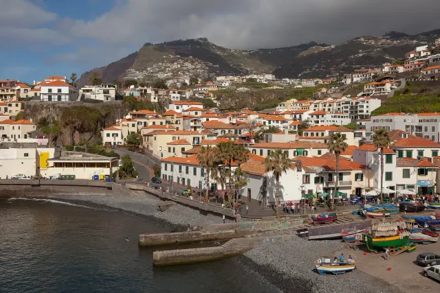 A fishing village of tiled roofs on a slope, colorful boats on a pebble beach