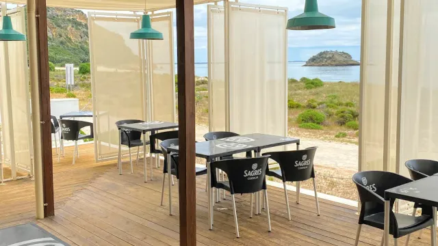 A covered wooden deck with tables and black chairs, and beyond it a shore and a small island