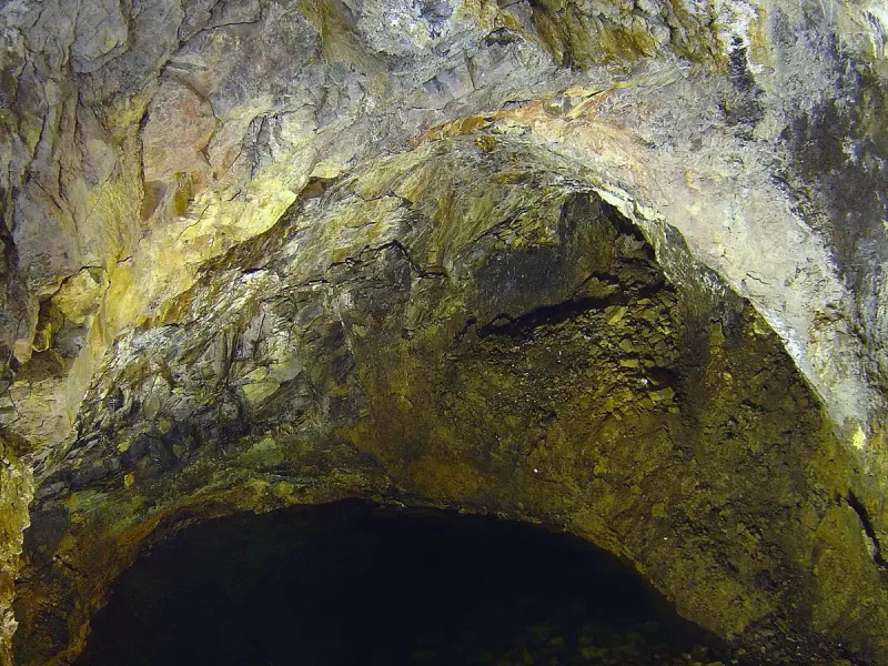 A volcanic rock vault in rust and yellow tones above a dark shaft