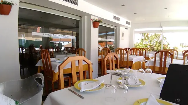 A bright hall with white tablecloths, yellow napkins and wooden chairs facing large windows