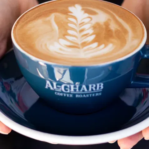 Hands holding a blue cup of latte with a leaf drawn in the foam