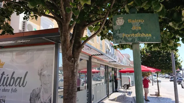 A street with a large tree, a green sign and covered stalls with red parasols