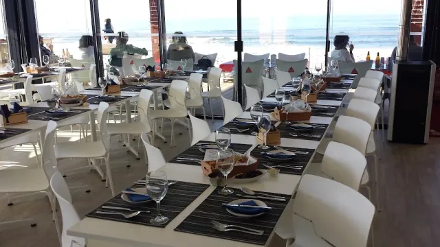 Long tables with white chairs facing a glass wall onto the beach and the sea